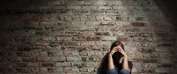 woman with head in her hands against brick wall